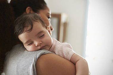 Eine Frau hält ihr schlafendes Baby auf dem Arm.