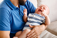 Ein Vater hält sein schreiendes Baby auf dem Arm.