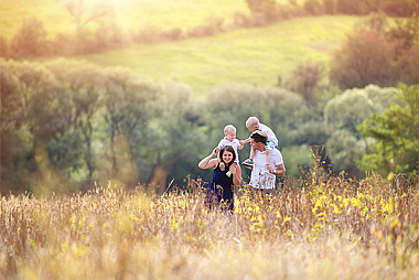 Vater und Mutter laufen mit ihren Kindern auf den Schultern durch ein Feld