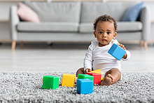 Ein Baby spielt auf dem Boden mit bunten Bauklötzen