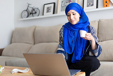 Eine Frau sitzt auf dem Sofa und schaut auf den Bildschirm ihres Laptops.