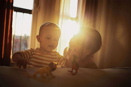 Babys und Kleinkinder reagieren besonders empfindlich auf Hitze Eine Mutter spielt mit ihrem Kind in der Wohnung. Hinter Vorhängen scheint die Sonne.