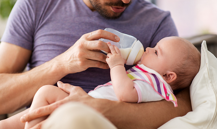 Ein Vater hält sein Baby im Arm und füttert es mit der Flasche