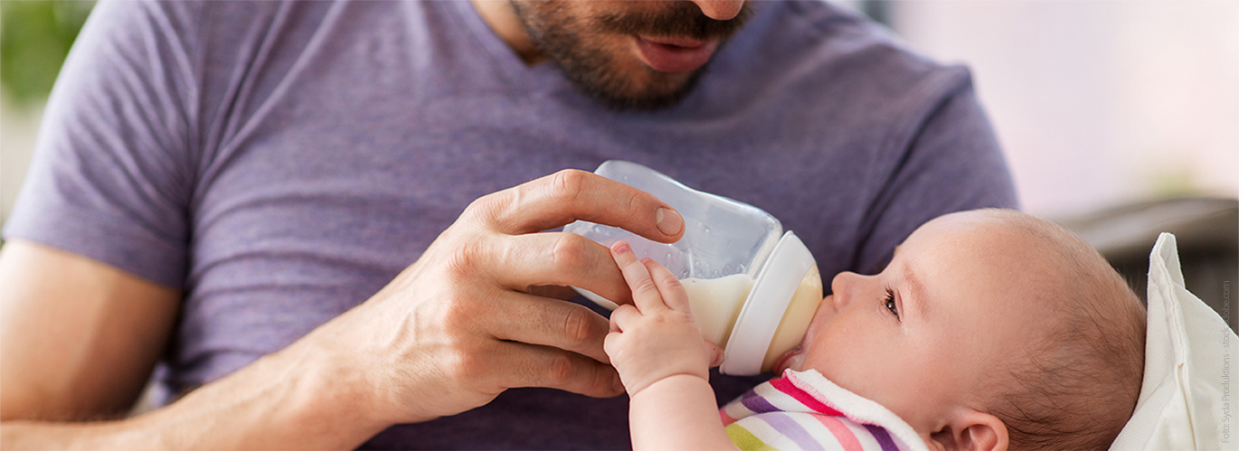 Ein Vater hält sein Baby im Arm und füttert es mit der Flasche