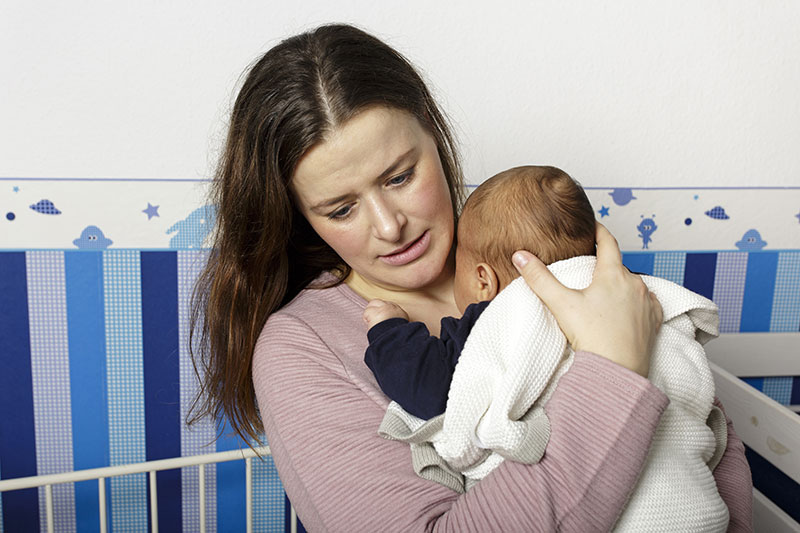 Gestresste Mutter hält Baby im Arm an sich gedrückt